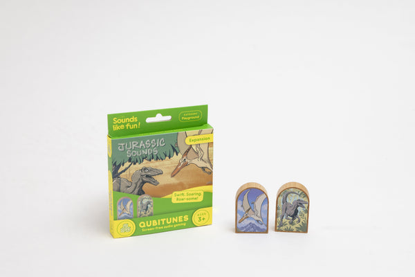 Qubitunes Jurassic Sounds plėtinio dėžutė ir dvi medinės kaladėlės su pterodaktiliu bei velociraptoriumi